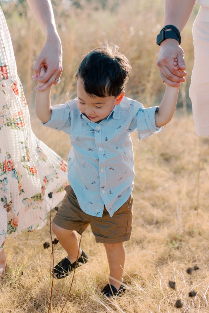 little boy walking holding parents hands at White Rock Lake Dallas TX by Kate White Photography