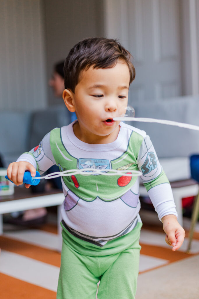 boy blows bubbles at family birthday party by Kate White Photography